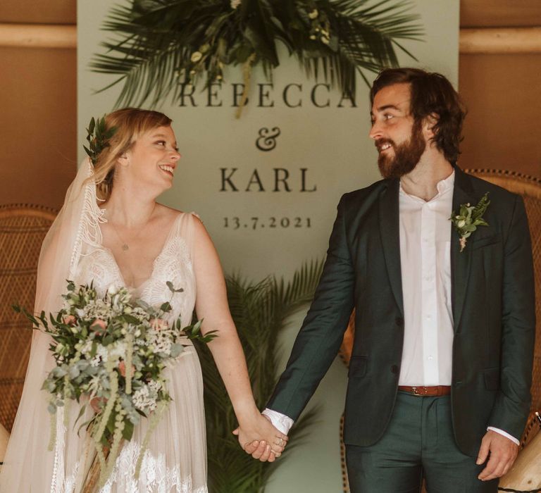 Bride & groom hold hands and look at one another inside tipi