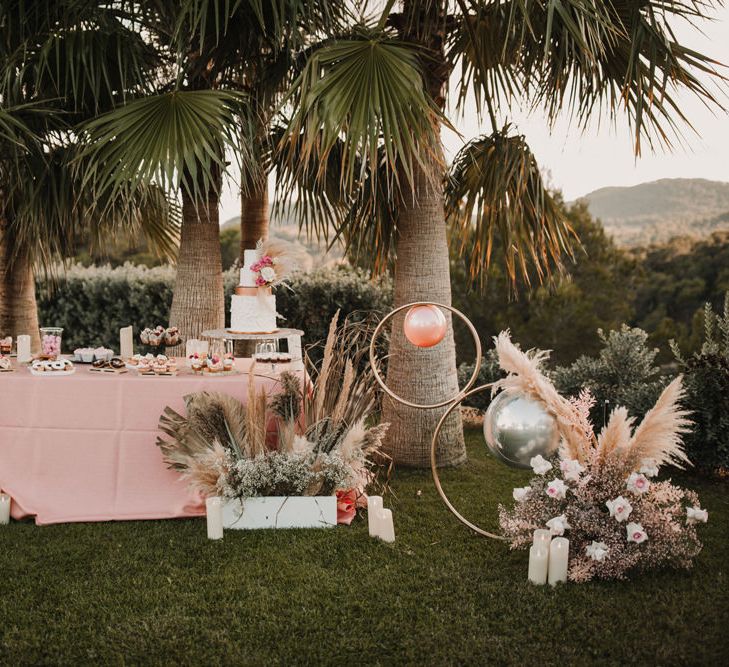 Cake table with pink table cloth, dried flowers and foil balloons 