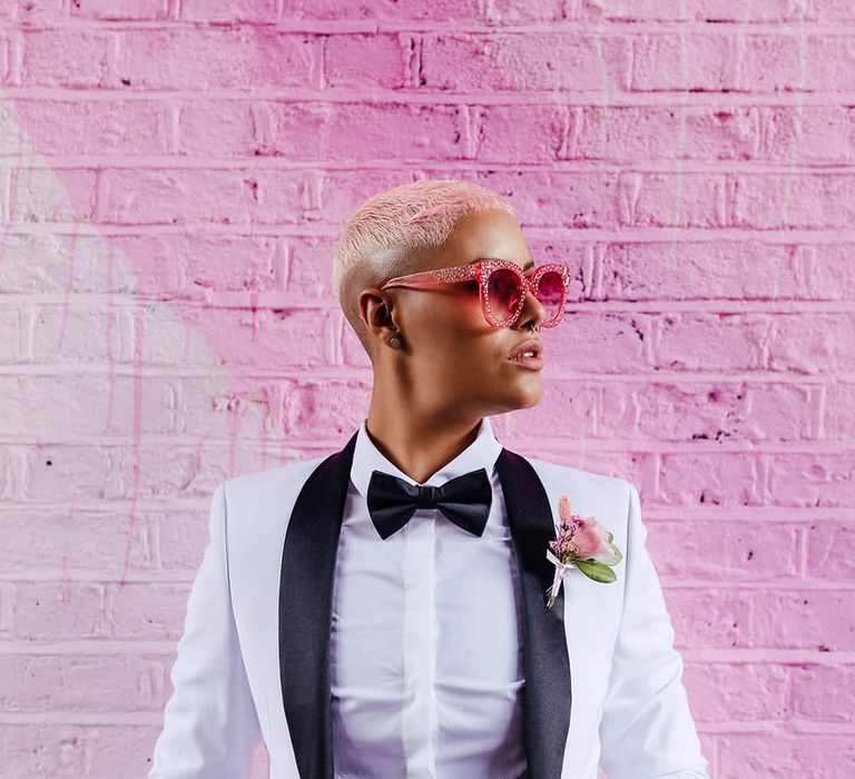 Stylish bride with short hair in a white tuxedo jacket and bow tie with pink sun glasses 