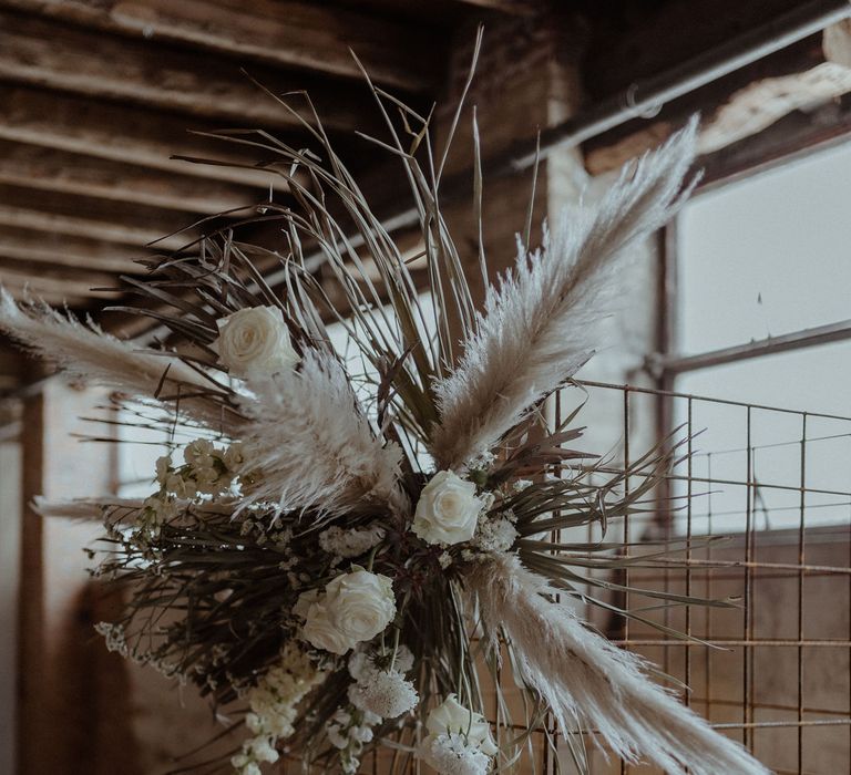 A metal structure forms a wedding altar. It is decorated with dried flowers and grasses in neutral tones for a simple elegant wedding. 