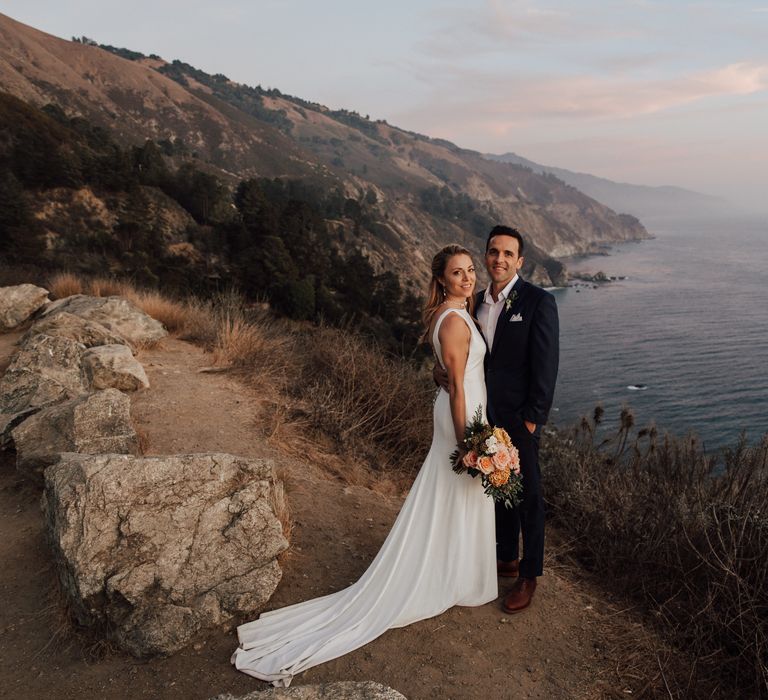 Bride & groom embrace one another on the cliffside 