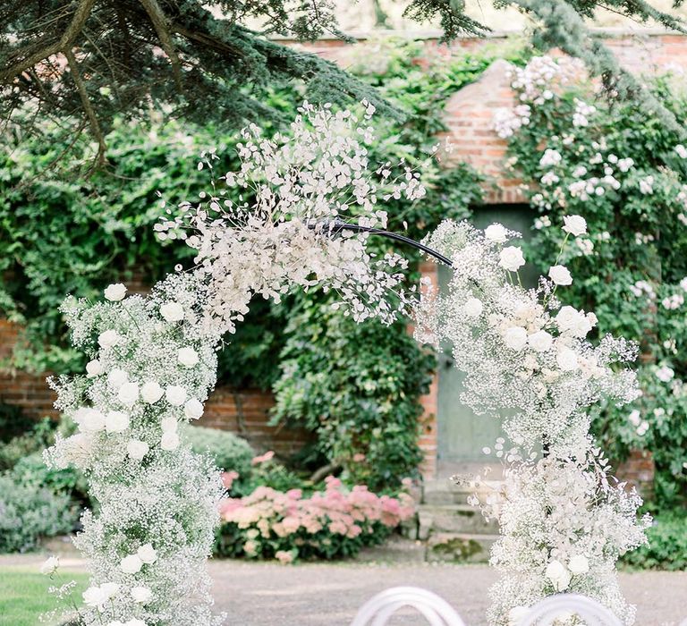 Outdoor ceremony at Garthymyl Hall wedding venue with white chairs and flower arch 