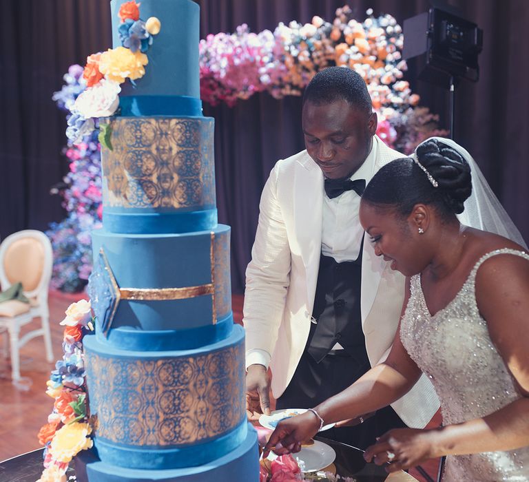 Bride & groom cut five tier wedding cake with blue & gold frosting