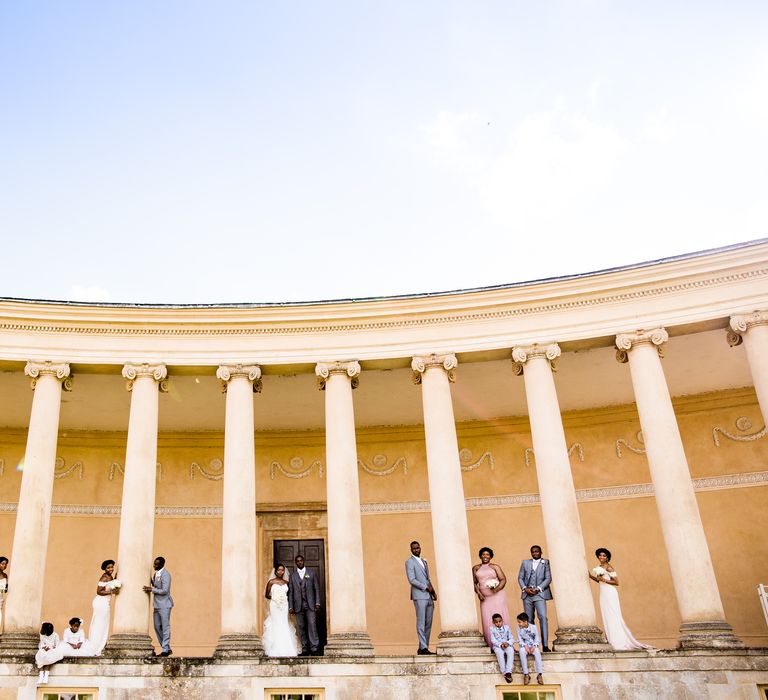 Wedding party stand beneath pillars on wedding day for post-wedding photoshoot