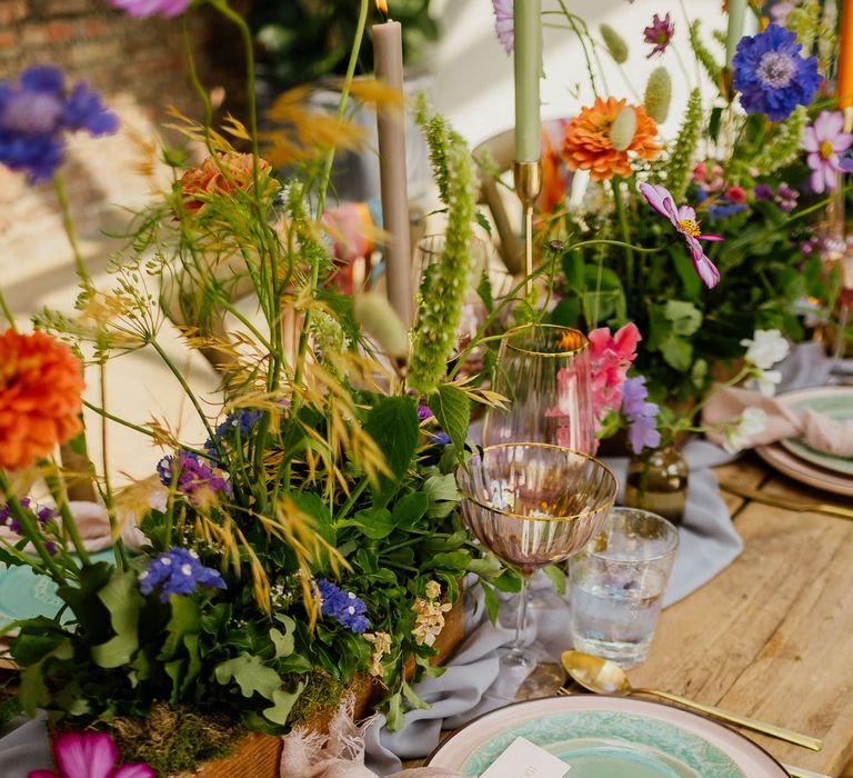 Place setting with pink and green tableware, table linen, wildflower centrepiece decor and iridescent glassware