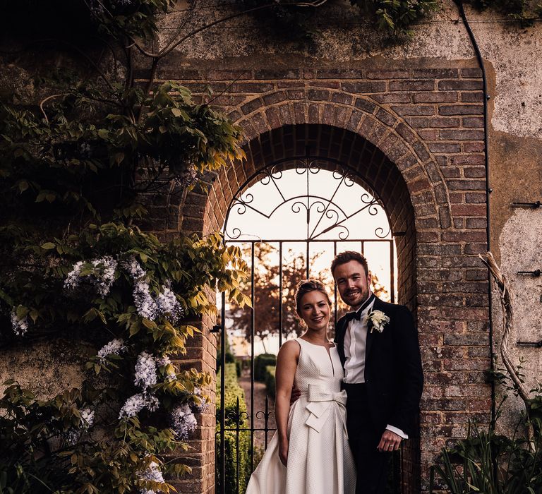 Bride & groom stand in front of metal gate on their wedding day