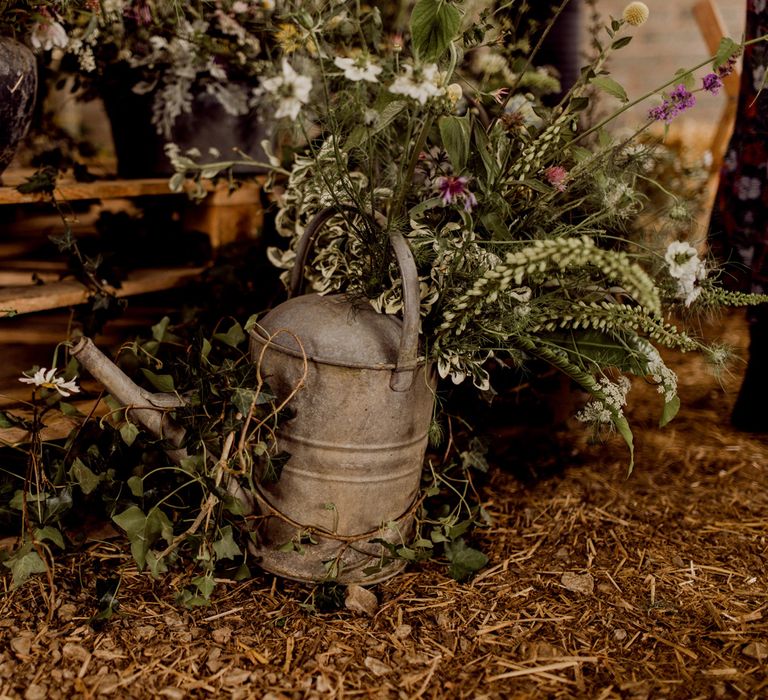 Metal watering can and wildflowers inside barn at home farm wedding 