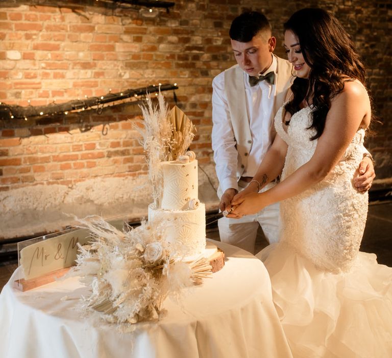 Bride and groom cutting their rustic wedding cake with dried flower decor and intricate design 