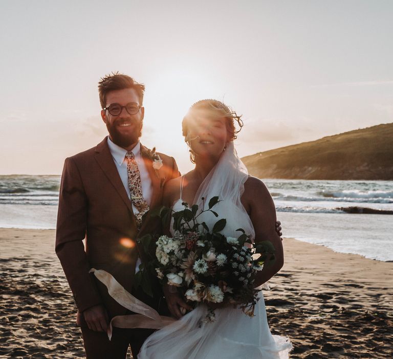 Bride & groom stand on the beach with one another on their wedding day for golden hour portraits