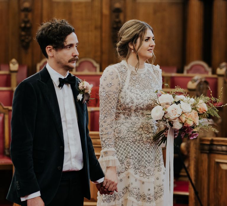 Bride & groom during wedding ceremony as bride wears her brown hair in loose curls for low up-do and carries floral bouquet