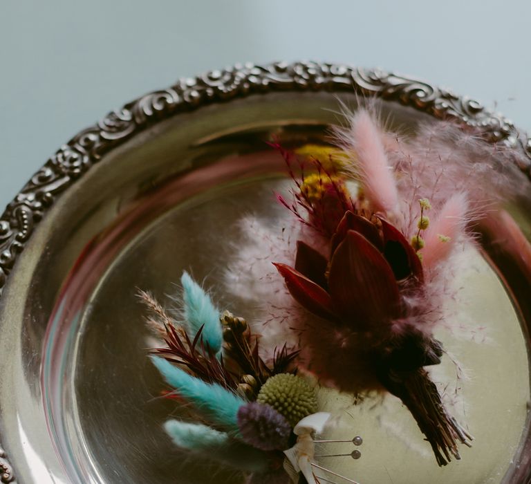 Brightly coloured pampas grass groom buttonhole on a gold platter 