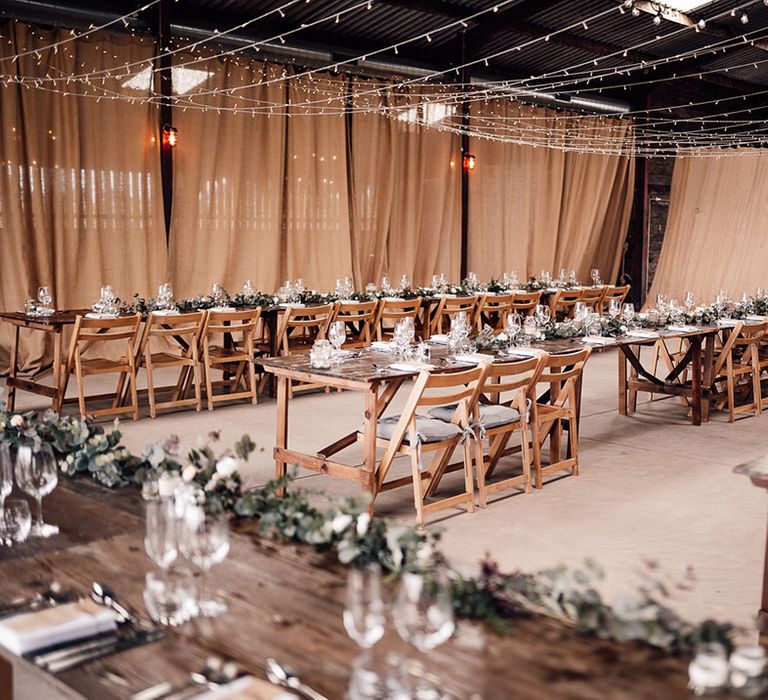 Fairy light canopy for rustic barn wedding with long wooden tables and faux foliage decor