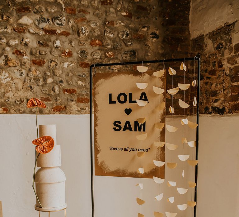 Contemporary wedding sign on a black metal stand with hanging garland next to the contemporary wedding cake display