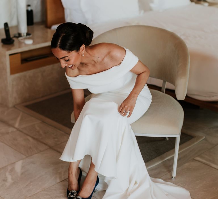 Bride puts on her shoes on her wedding day as she sits down | Hannah MacGregor Photo & Film