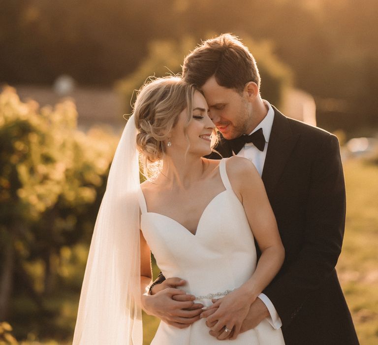 Intimate golden hour bride and groom portrait with bride in a Stella York wedding dress with cathedral length veil and groom in a tuxedo 