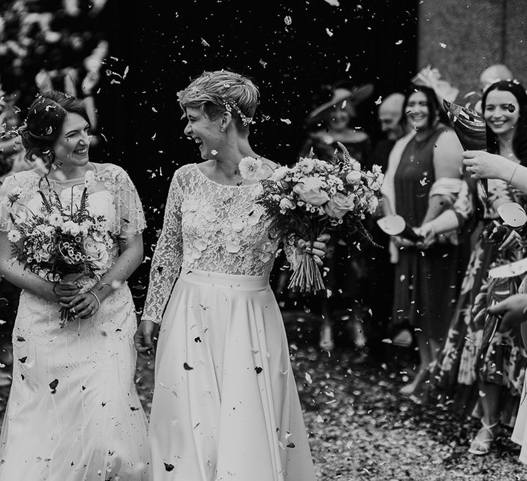 Black and white confetti wedding photograph with two brides looking and smiling at each other 