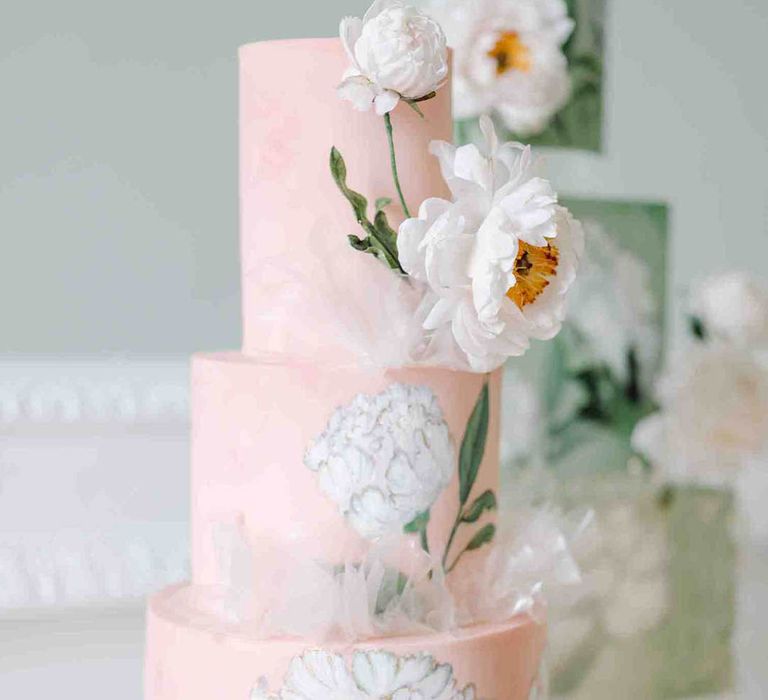 Light pink three-tier wedding cake with white flower illustration on a glass cake stand 