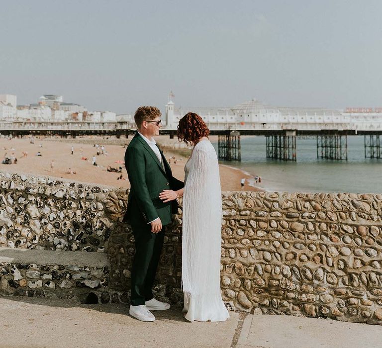 Bride & groom stand beside brick wall by the seaside beach front in Brighton on their wedding day