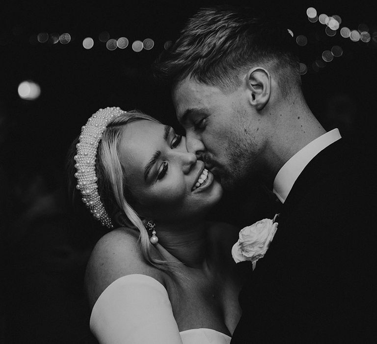 black and white portrait of the groom kissing his brides cheek as she wears a pearl decorated headband 