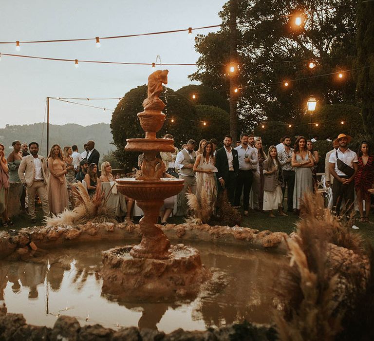 Wedding guests gather outdoors in front of fountain