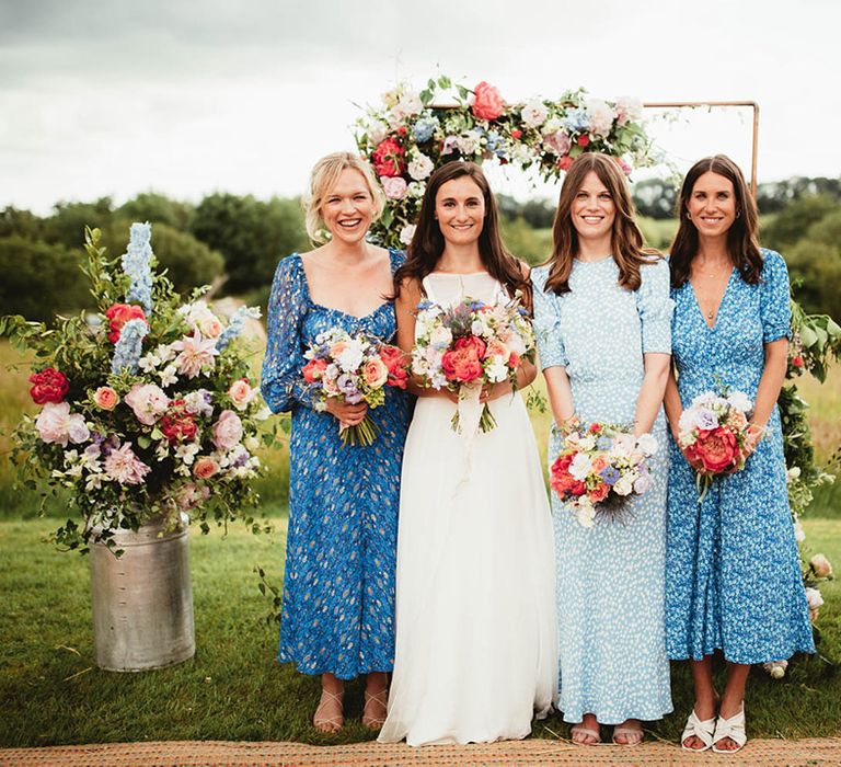 Bride stands with her bridesmaids who wear pale blue dresses in differing styles 