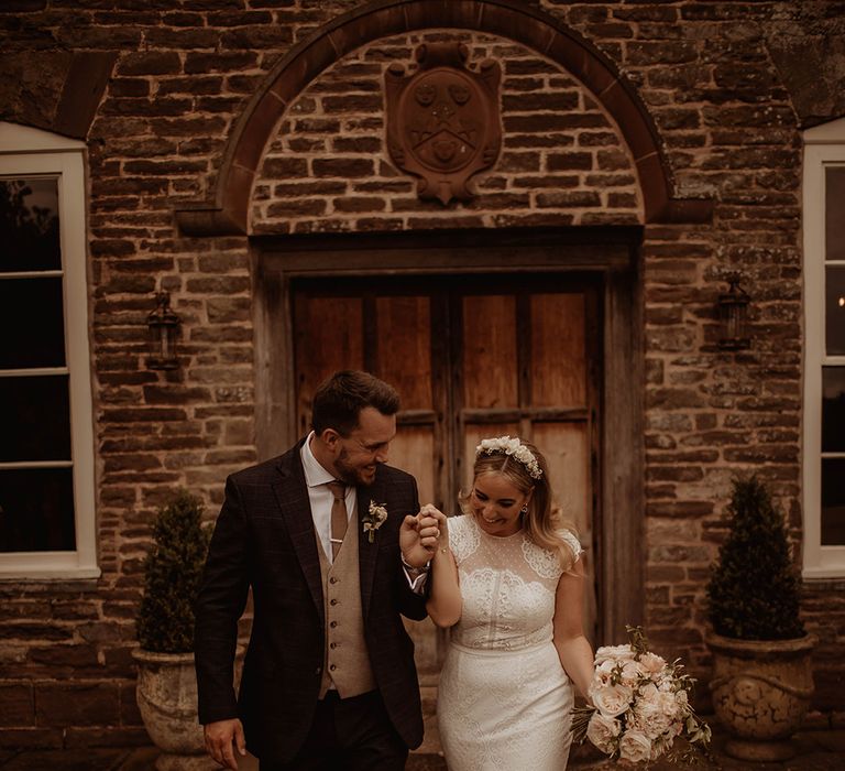 Bride in a lace cap sleeve wedding dress with mermaid skirt and groom in a three-piece suit holding hands at their Dewsall Court wedding 