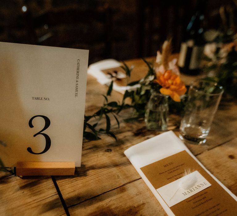 Simple table number sign with rustic stationery, foliage table garland and orange florals for wedding reception