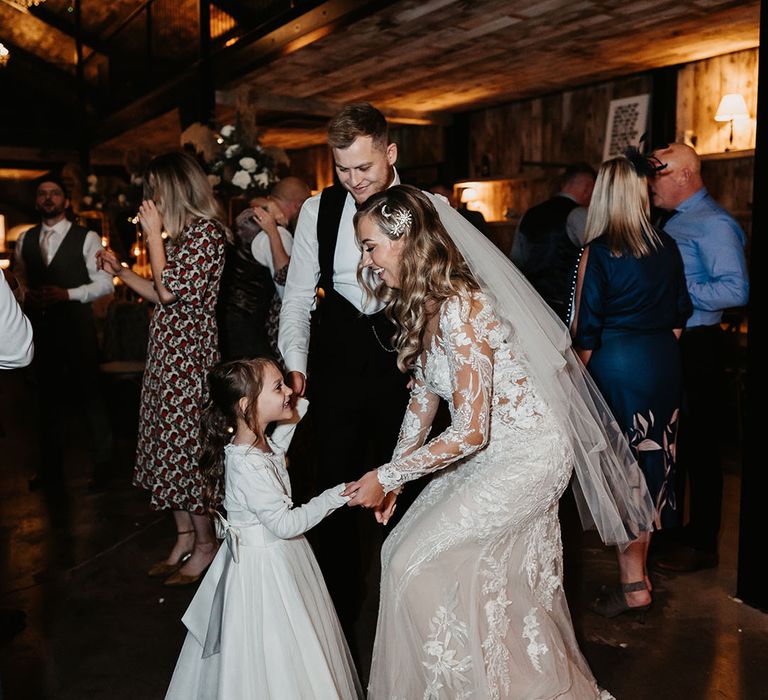 Bride in lace dress and moon and star hair accessories dances with flower girl as groom watches