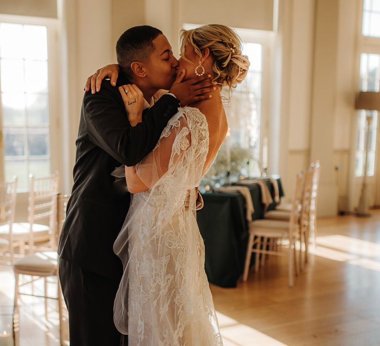 LGBTQI+ couple kissing wearing a black suit and applique wedding dress 