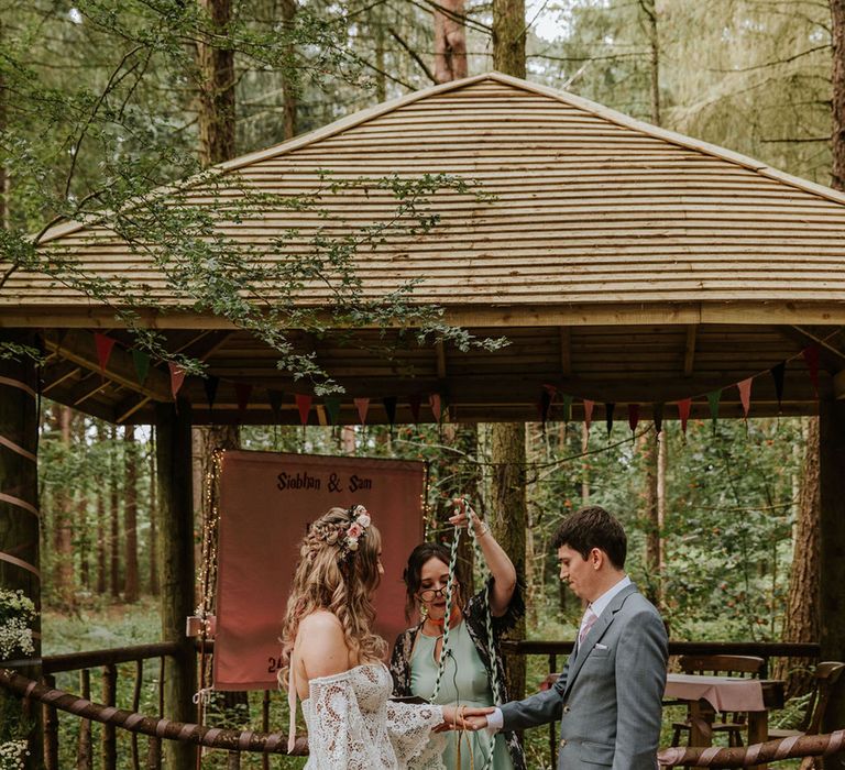 Bride and groom participate in woodland outdoor handfasting ceremony for fantasy themed wedding 