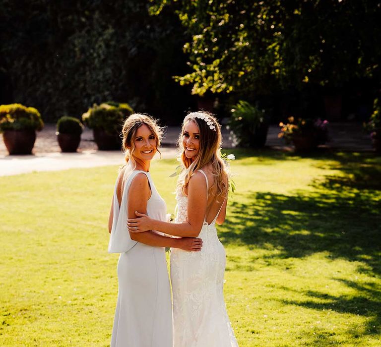 Bride in lace wedding dress with train and veil holding the arm of bridesmaid in grey low back dress