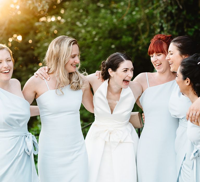 Bride smiles and laughs with bridesmaids in different style dresses in baby blue shade 