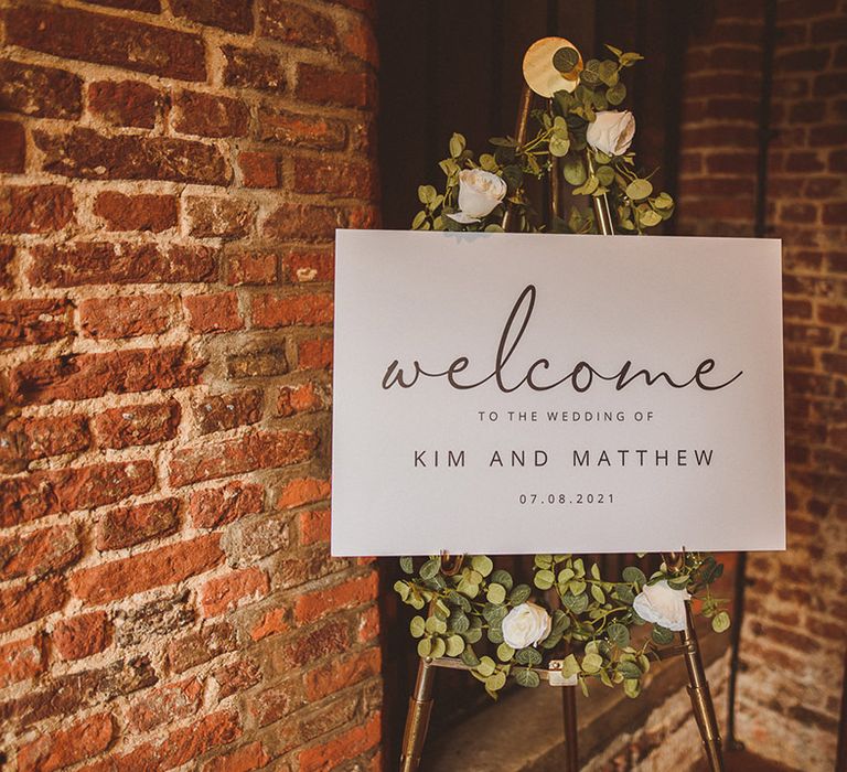 Simple black and white welcome wedding sign on easel decorated with classic white and green wedding flowers 