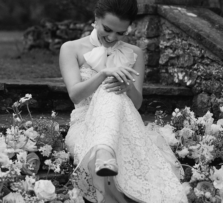 Bride in a strapless lace wedding dress and satin neck scarf sitting on the steps at Holesfoot