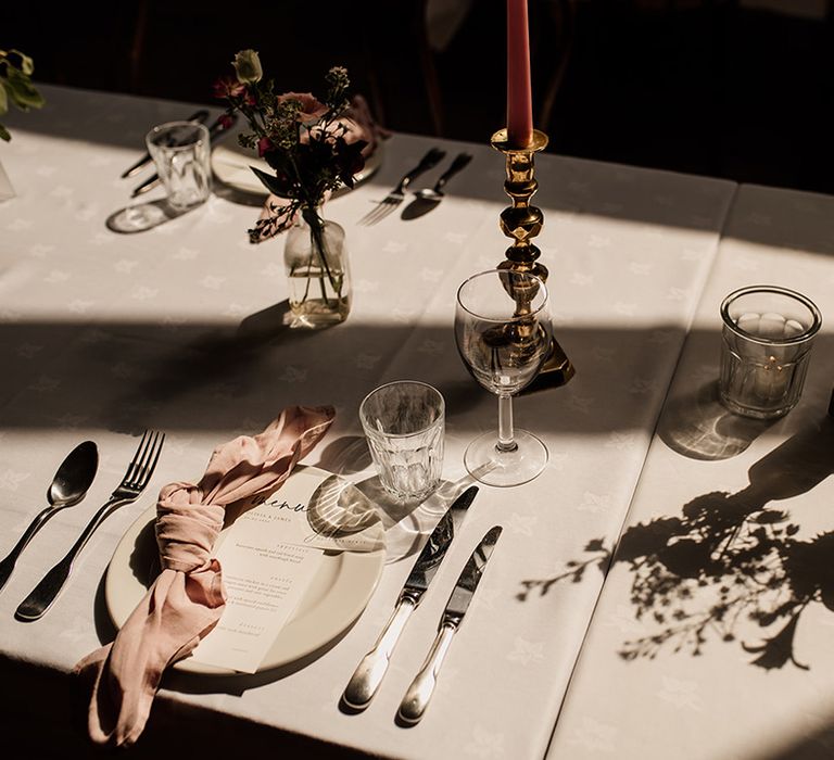 Plain white plates, tablecloth and menu card with pink napkins and pink candles in gold holders