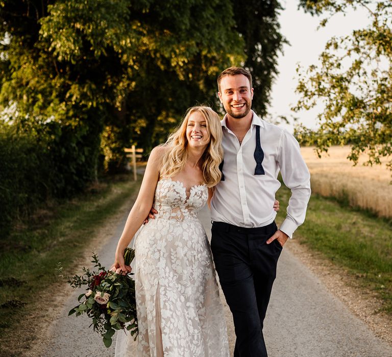 Groom walks with his arm around the bride with his bow tie undone and bride wears a strapless lace wedding dress 