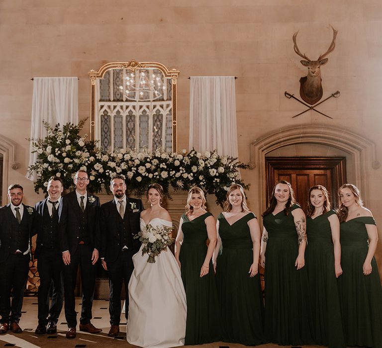 Wedding party with bride and groom and bridesmaids in green dresses and groomsmen in three piece dark blue suits