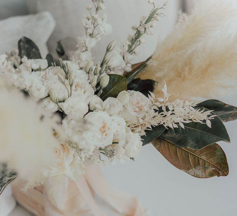 Bridal bouquet filled with pampas grass and green foliage tied with white ribbon 