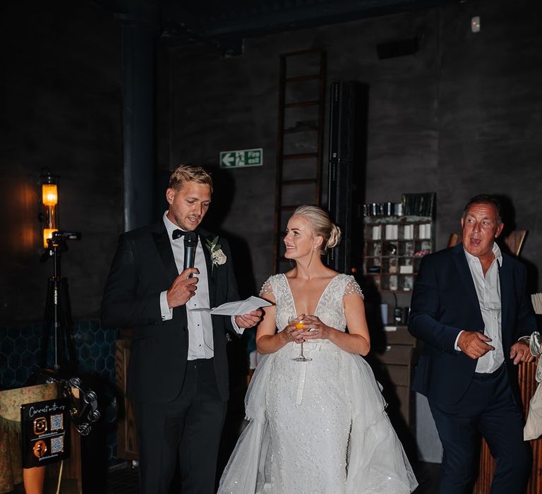 Groom in black tie gives wedding speech during reception at Speakeasy on their wedding day