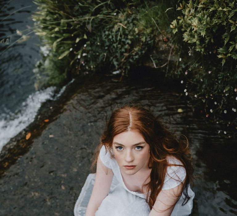 Beautiful bride with long hair and natural makeup sitting in the moat at Bishop's Palace, Wells