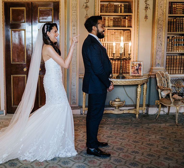 Bride wears lace fitted mermaid wedding dress with cathedral veil as she stands behind her groom for first-look moment at Syon Park