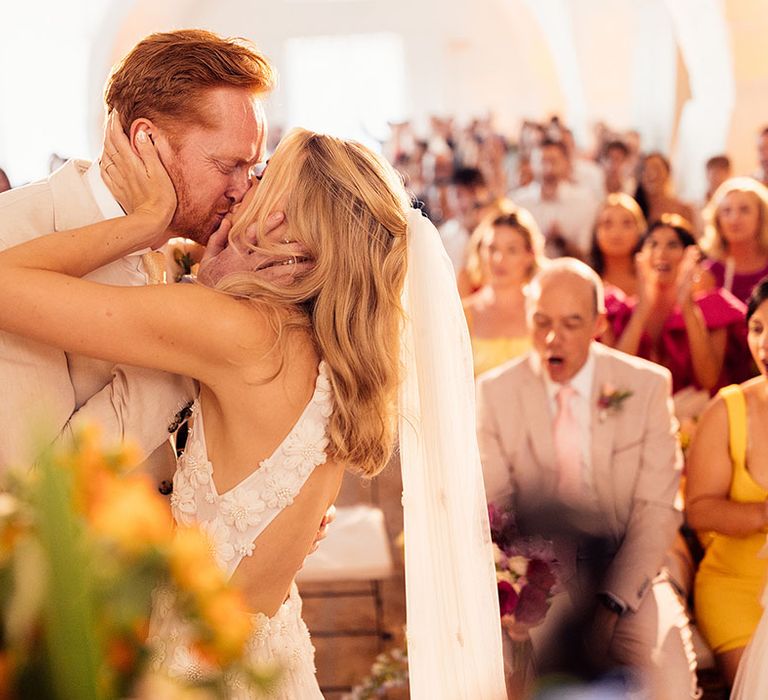 Bride and groom share their first kiss as a married couple as the wedding guests cheer 