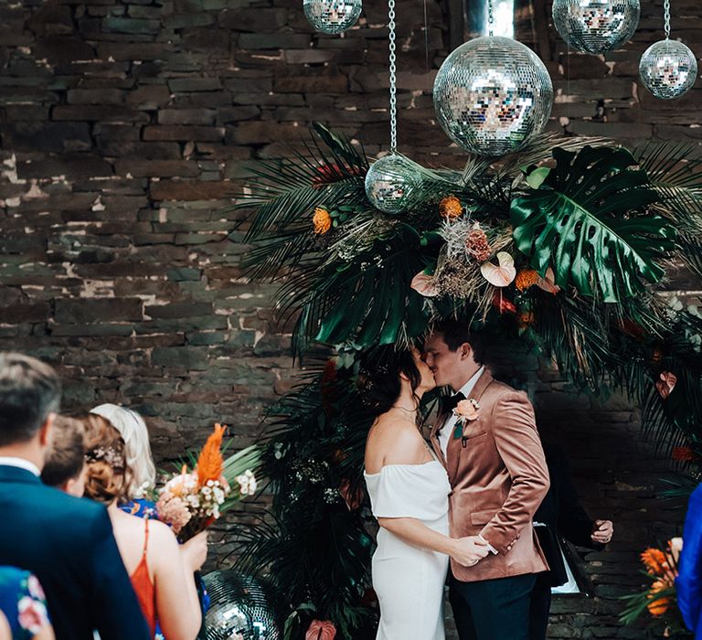 Bride and groom share their first kiss as a married couple with disco balls and a tropical moon gate