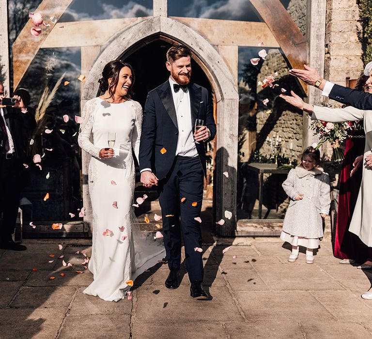 Bride in long sleeve Pronovias wedding dress having confetti exit with the groom in black tie 