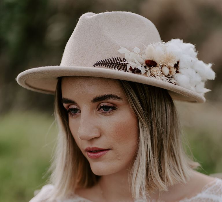 Bride with a sun-kissed bronze makeup look wearing a wedding hat with dried flowers and cotton 