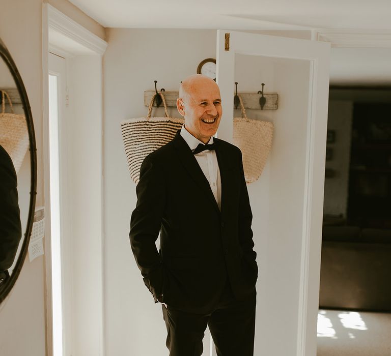 Father of the bride in black tie smiling brightly as he sees the bride in her wedding dress for the first time 