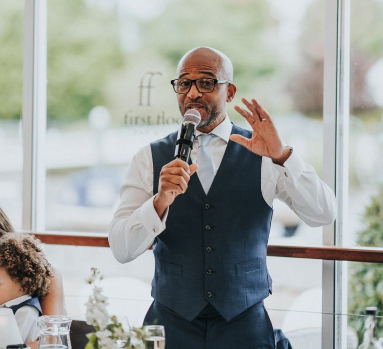 Wedding guest in blue waistcoat and white shirt gives speech during reception