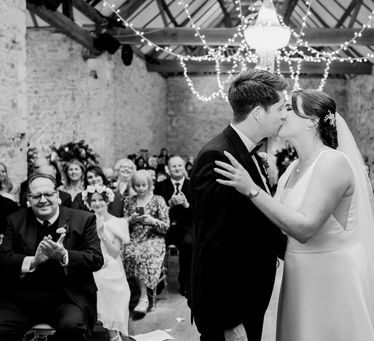 The wedding guests clap as the bride and groom share their first kiss as a married couple 