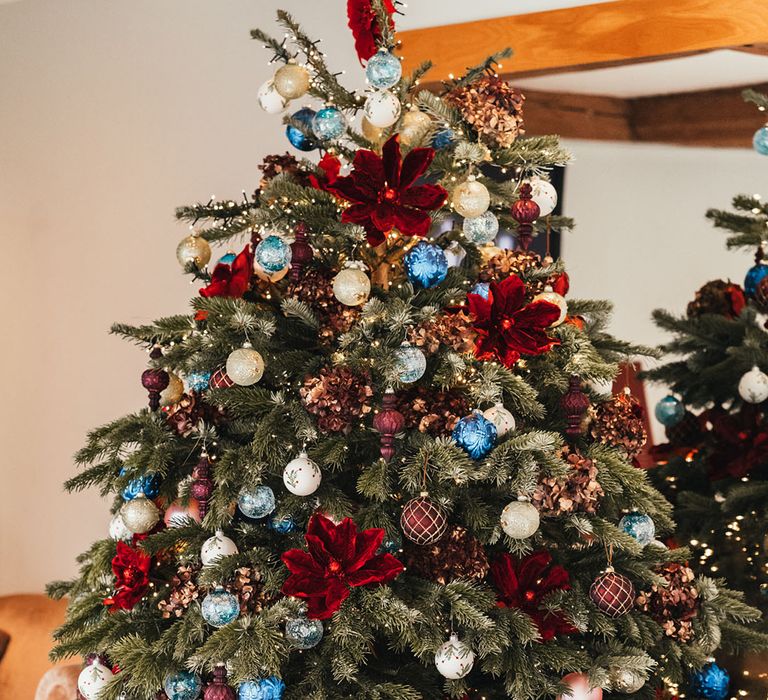 Christmas tree decorated with gold, silver, and blue baubles with red poinsettia decor for the winter Christmas wedding 