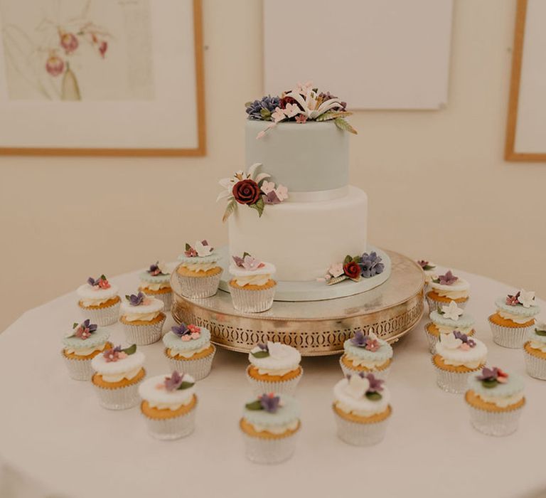 Two tier pastel wedding cake surrounded by mini pastel cupcakes finished with fondant floral design